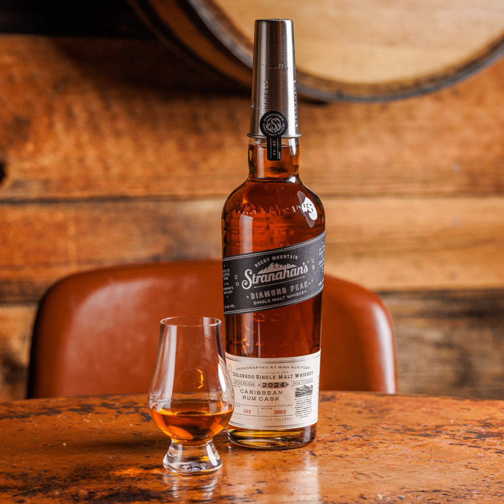 Bottle of Stranahan's Diamond Peak Caribbean Rum Cask paired with a dram of the whiskey on a table surface