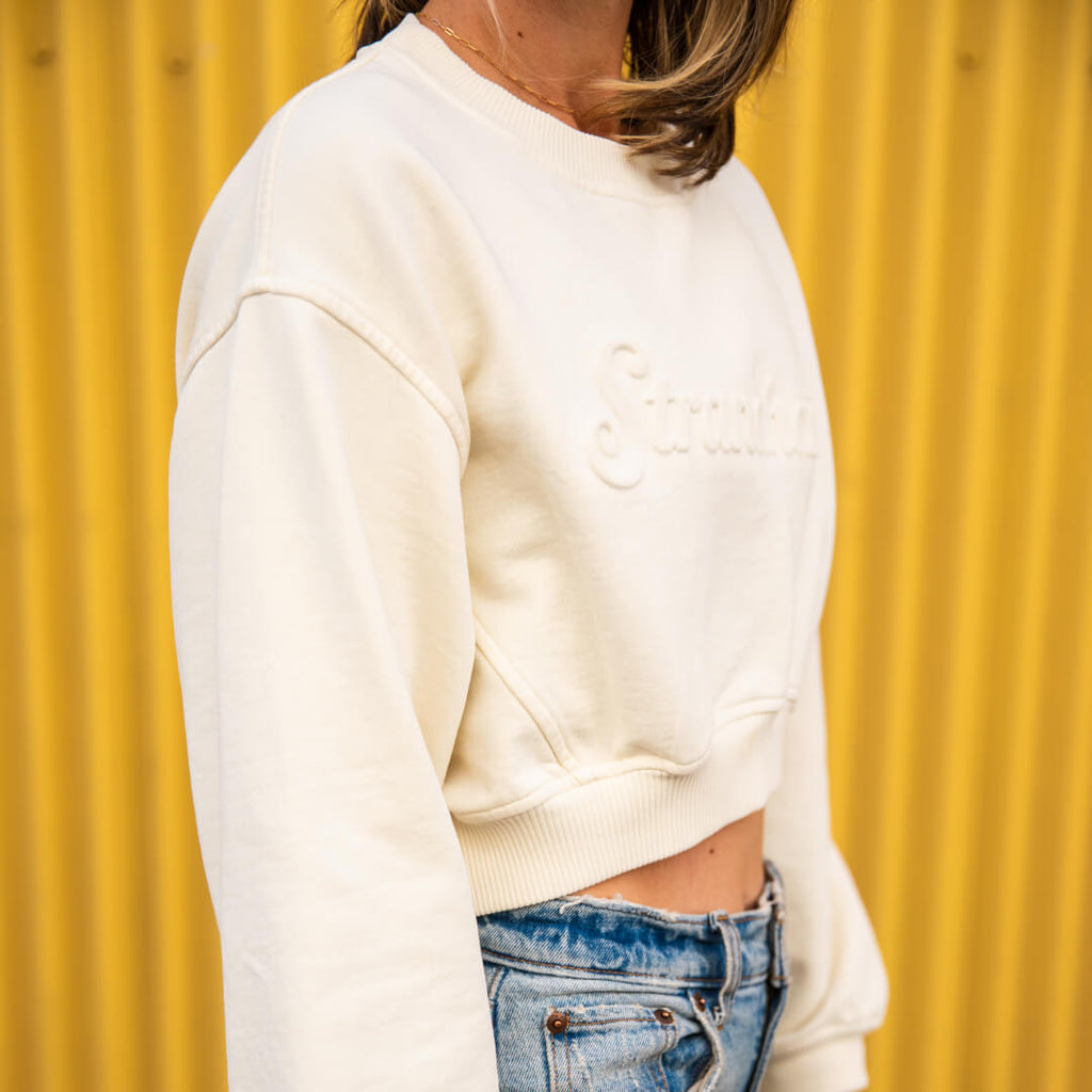 Side view of woman wearing cream-colored cropped sweatshirt embossed with Stranahan's logo