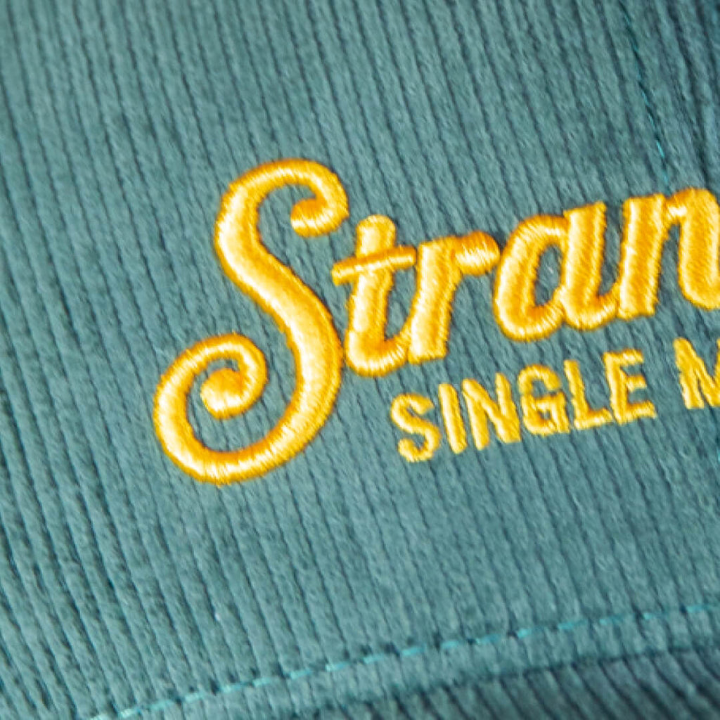 Closeup of yellow embroidered Stranahan's logo and 'Single Malt Whiskey' on Green Corduroy Hat