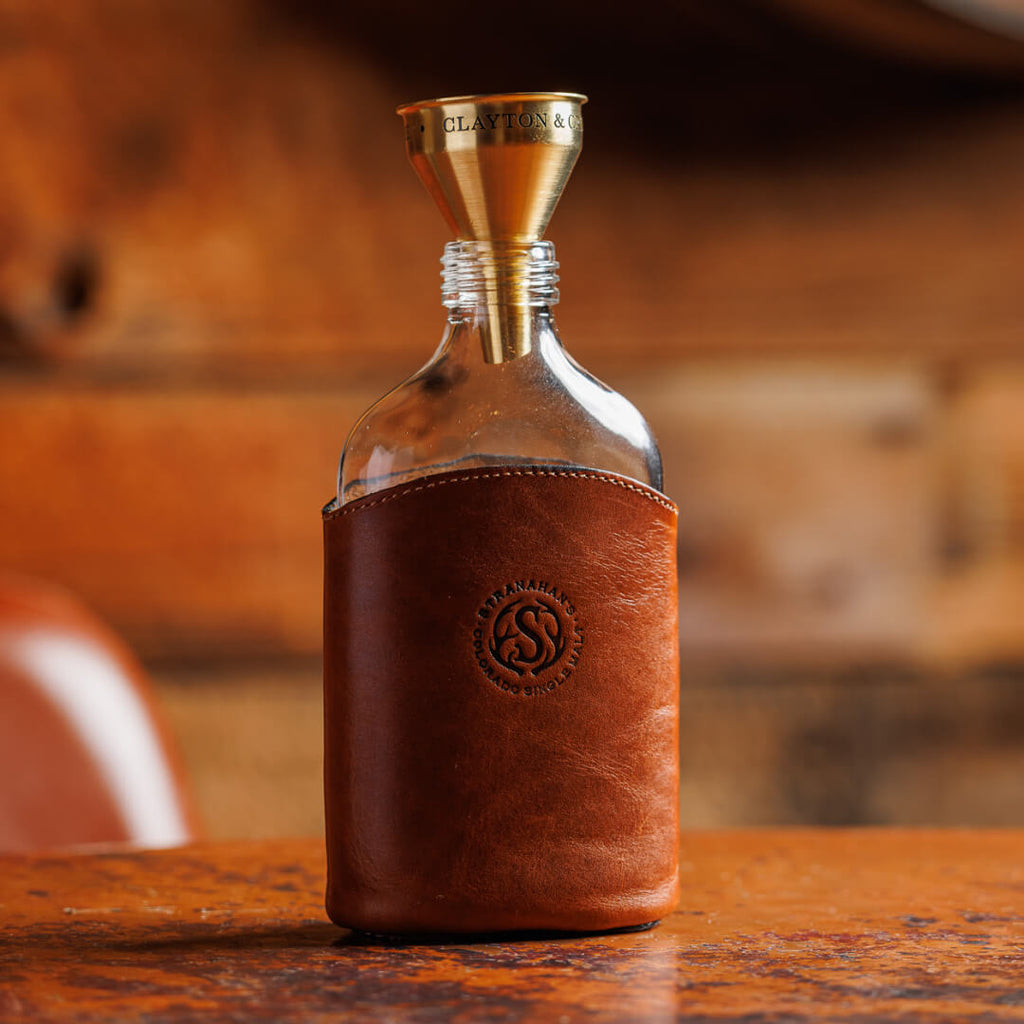 Unscrewed Leather Glass Flask stamped with the Stranahan's logo with funnel placed within the neck of the flask