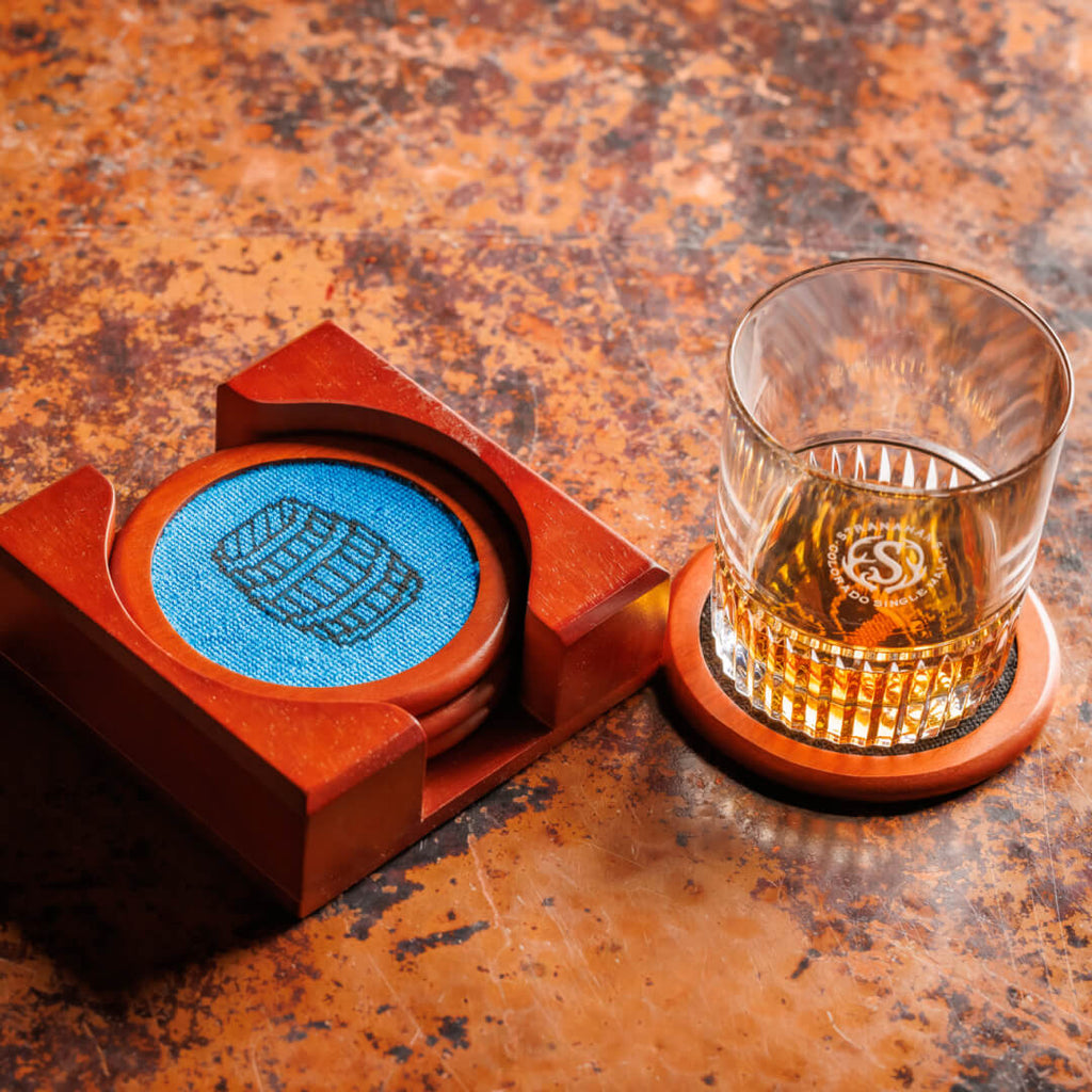 Set of 4 Stranahans x Smathers & Branson Needlepoint Coasters in a wooden holder, next to a pour of Stranahan's American Single Malt.