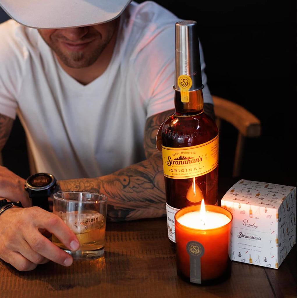 Man enjoying a pour of Stranahan's Original, next to Stranahan's X Sunday Candle Co. Colorado Reserve Candle in amber glass vessel