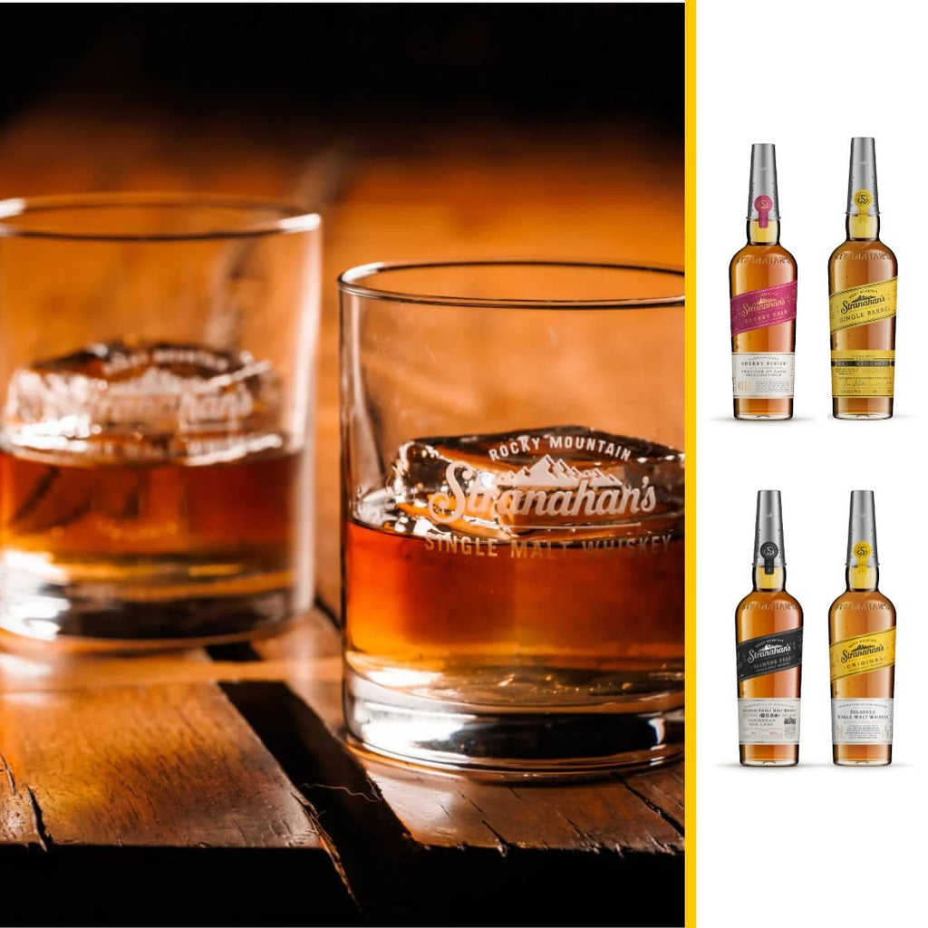 Two glasses of Stranahan's Single Malt Whiskey with the Rocky Mountain logo on a wooden surface, alongside a selection of Stranahan's whiskey bottles displayed on the right.