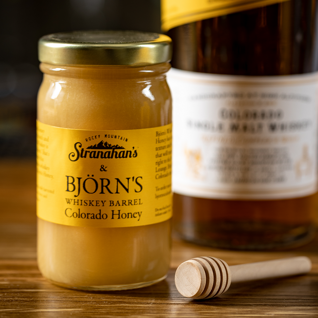 Close up of Stranahan's whiskey barrel Colorado honey and wooden honey want with Stranahan's Original Whiskey out of focus in the background.