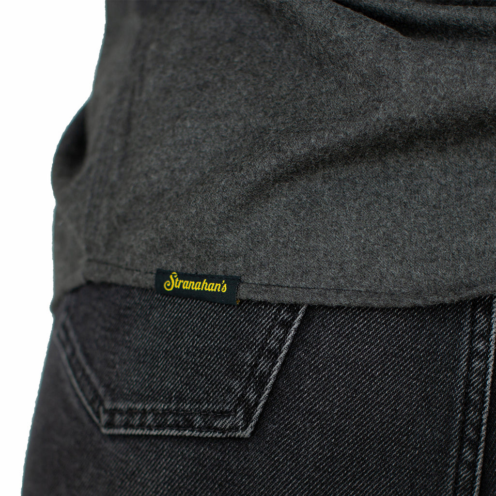 Close up of Stranahan's logo on the back hem of dark grey button down shirt.