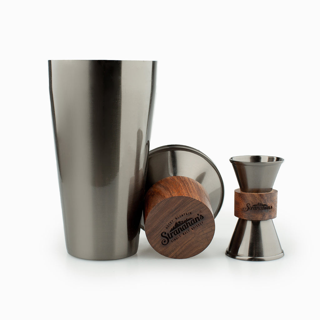 Stranahan's wood and gunmetal cocktail shaker and jigger on white background.